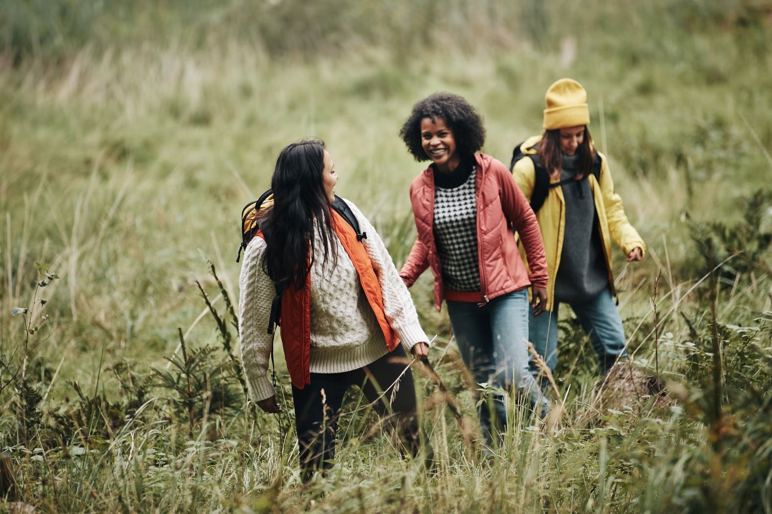 Three friends happily walk through a grassy field on a hike.